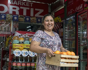 Smiling woman standing outside storefront with Coca-Cola advertisements